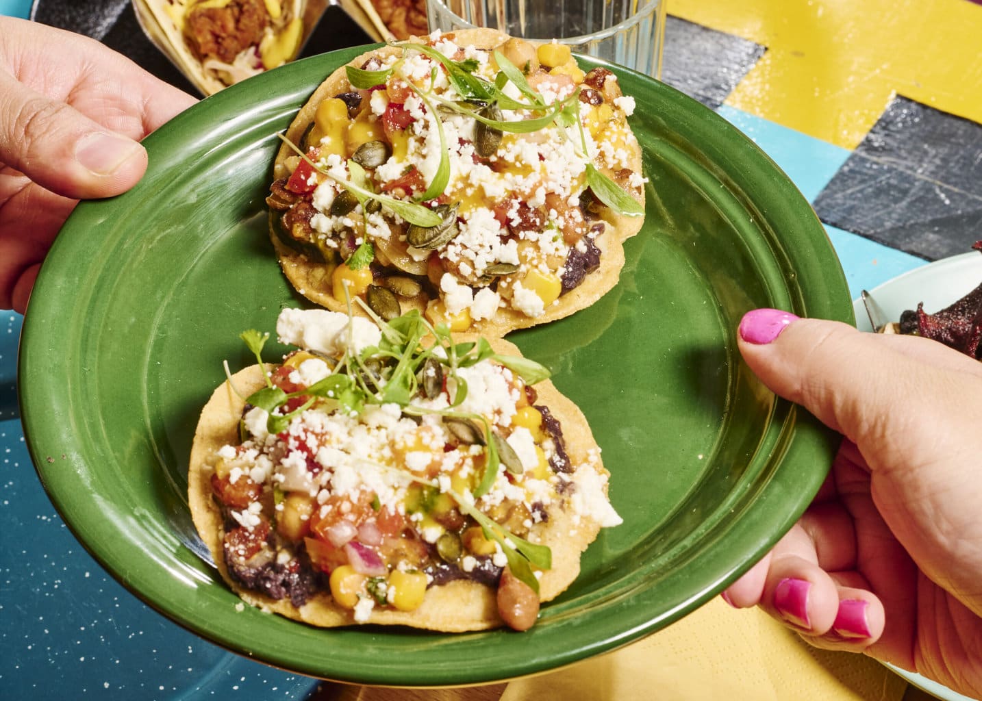 A plate of zesty bean tostadas being passed across a table