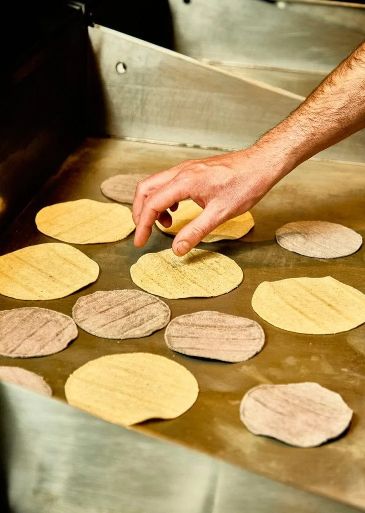 Soft corn tortillas for our tacos heat up on the hot plate in the kitchen while a chef watches over and turns them