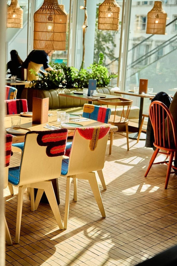 Tables in our Mexican restaurant in London Paddington. The restaurant has plent of natural light and colourful pops from the handmade artisan chair covers. Natural touches come from additions of indoor plants and wooden lampshades, as well as natural light from the floor to ceiling windows.