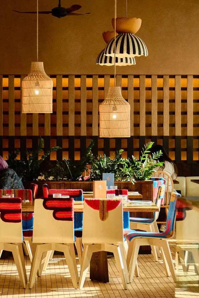 The inside of our Mexican restaurant in London Paddington. A long table that seats 12 people is drenched in natural light. Chairs with artisan woven chair covers bring a pop of colour to the restaurant, while low hanging lights provide a sense of intimacy.