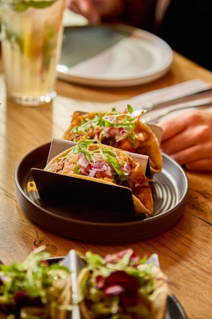 A plate of Mexican beef gringa tacos sit on a table in our Mexican restaurant in London. The tacos are grilled with cheese and topped with fresh tomato salsa and micro herbs.